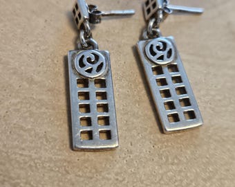 May include: A pair of silver dangle earrings with a geometric design. The earrings feature a square top with a small circle in the center and a rectangular pendant with a grid pattern.