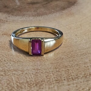 May include: A gold ring with a rectangular purple gemstone set in a bezel setting. The ring is marked "925" on the inside band.