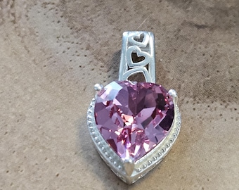 Peut inclure: Un pendentif en argent avec une pierre précieuse en forme de cœur rose. Le pendentif a un design délicat avec de petits cœurs autour de la pierre précieuse.
