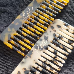 May include: Two tortoiseshell combs with personalised engravings. The top comb has the name "Lei" engraved on it, and the bottom comb has the name "Bea" engraved on it.