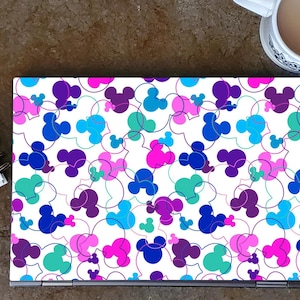 May include: A white laptop skin with a repeating pattern of colorful Mickey Mouse heads. The heads are outlined in white and filled with shades of blue, pink, purple, and green.