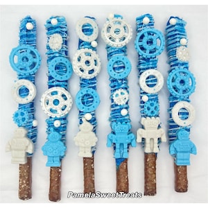 May include: A set of six chocolate-covered pretzel rods decorated with blue and white chocolate. The pretzels are topped with white chocolate robot figures and blue and white chocolate gears.