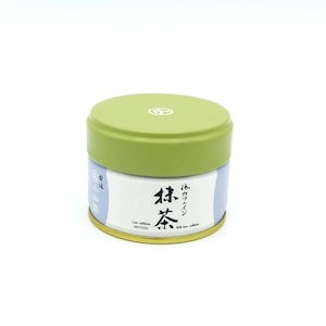 Könnte beinhalten: Eine runde Dose Matcha-Tee mit grünem Deckel. Die Dose hat japanischen Text und das englische Wort "Matcha" auf einem weißen Etikett. Der Korpus der Dose ist hellblau und goldfarben.