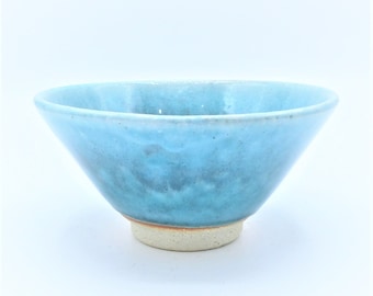 May include: A light blue ceramic bowl with a speckled glaze. The bowl has a wide rim and a rounded base.