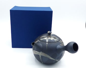 May include: A black ceramic teapot with a silver glaze design. The teapot has a round body and a short spout. The teapot is sitting on a blue box.
