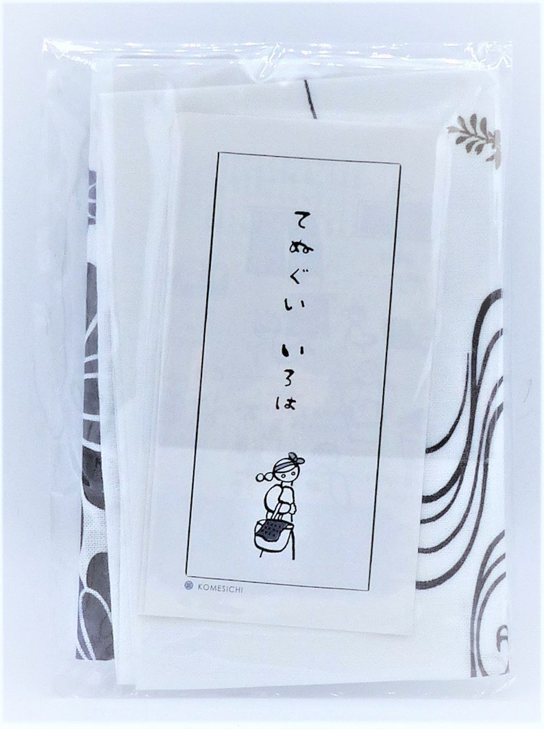 Puede incluir: Un paquete que contiene una tela blanca y negra estampada y una tarjeta blanca con texto japon&eacute;s y una ilustraci&oacute;n de dibujos animados de una persona que lleva una cesta. La tela tiene un dise&ntilde;o floral.