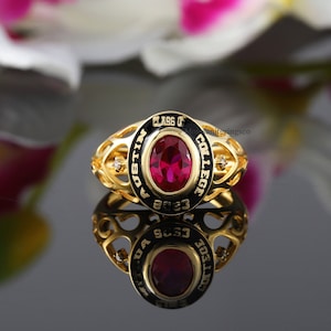 Może przedstawiać: Złoty pierścionek klasowy z czerwonym kamieniem szlachetnym i czarną emalią. Na pierścionku widnieje napis "Austin College Class of 2023".