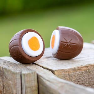 Peut inclure: Deux œufs en chocolat, l'un coupé en deux pour révéler une garniture de bonbons blanche et orange. Les œufs sont posés sur une surface en bois.
