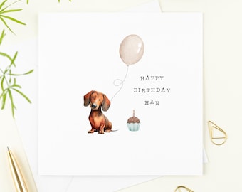 May include: A white birthday card with a watercolour illustration of a dachshund, a balloon, and a cupcake. The card reads "HAPPY BIRTHDAY HAN". The dachshund is brown and tan, and the cupcake is blue with a lit candle.