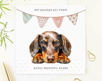 Puede incluir: Tarjeta de felicitación con una ilustración de acuarela de un perro salchicha. La tarjeta tiene el texto "DID SOMEONE SAY CAKE?" encima del perro y "HAPPY BIRTHDAY LAURA" debajo. La tarjeta está decorada con banderines en colores pastel.