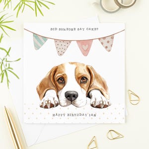 May include: A birthday card with a beagle illustration. The dog has brown and white fur and is looking at the viewer. The card has the text "DID SOMEONE SAY CAKE?" above the dog and "HAPPY BIRTHDAY IAN" below.