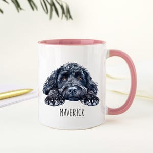 May include: White ceramic mug with a pink interior and handle. The mug features a detailed illustration of a black dog with the name "MAVERICK" printed below the dog. The mug is a standard size for coffee or tea.