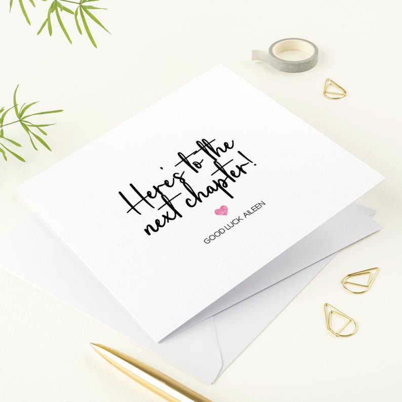 K&ouml;nnte beinhalten: Eine wei&szlig;e Karte mit schwarzer Kalligraphie, auf der "Here's to the next chapter!" steht, mit einem rosa Herzen und dem Text "Good Luck Aileen" darunter.
