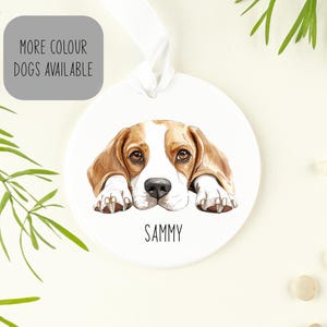 May include: White ceramic ornament featuring a watercolour illustration of a Beagle dog with brown and white fur. The dog is lying down with its head resting on its paws. The ornament has the name "Sammy" written below the dog.