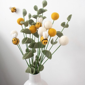 May include: A bouquet of felt flowers in white and yellow with felt bees. The flowers are arranged in a white vase.