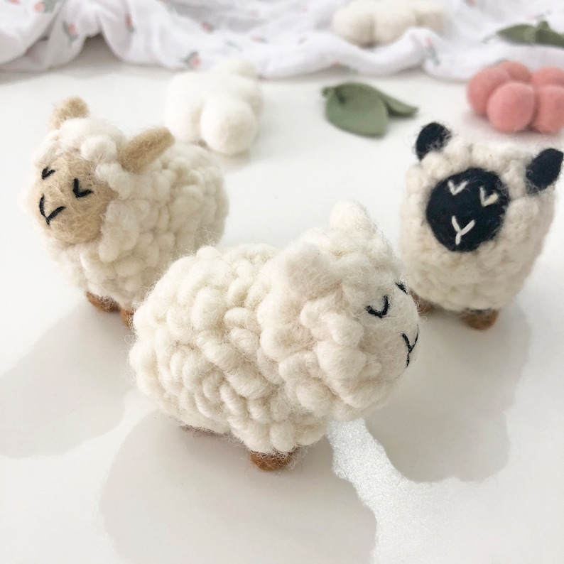 May include: Two white felt sheep toys. One sheep has black eyes and a black nose. The other sheep has brown eyes and a brown nose.