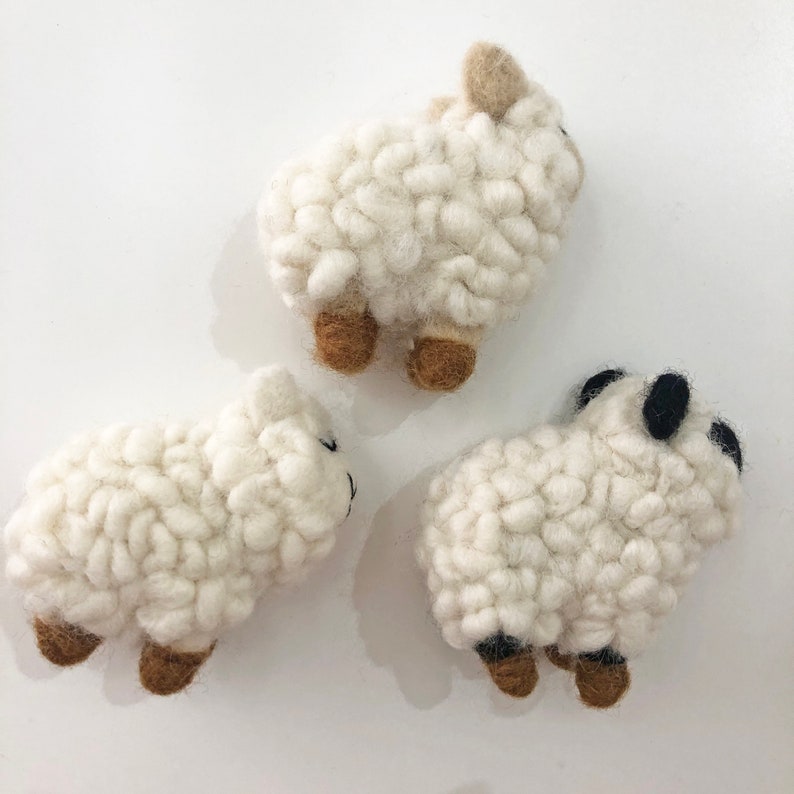 May include: Three white felt sheep toys with brown legs and black eyes. The sheep are all different sizes and are arranged in a triangular shape.