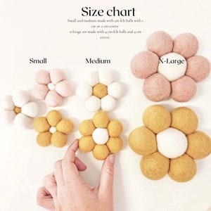 May include: A size chart displays felt flower decorations in small, medium, and x-large sizes. The flowers are made of felt balls in white, pink, and yellow. The text on the chart indicates the size and construction details.