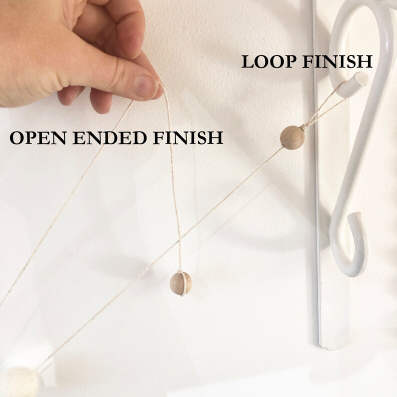 May include: A close-up of a decorative garland with wooden beads and a loop finish. The garland is suspended against a white wall. The text "OPEN ENDED FINISH" and "LOOP FINISH" are visible.
