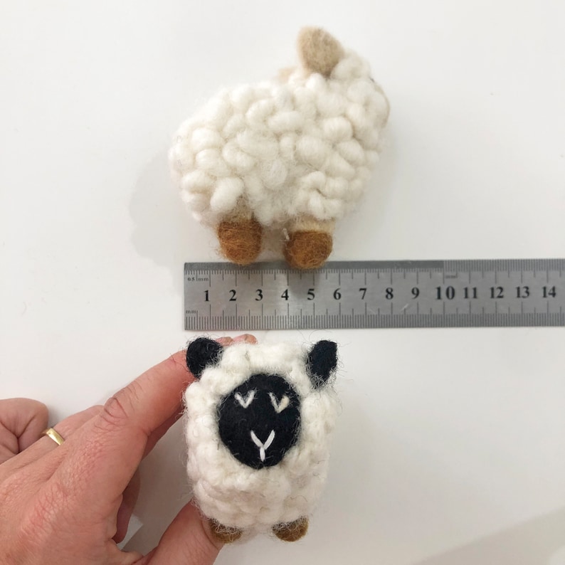 May include: Two white felt sheep toys. One sheep has a black felt face with white stitching. The sheep are approximately 4 inches tall.