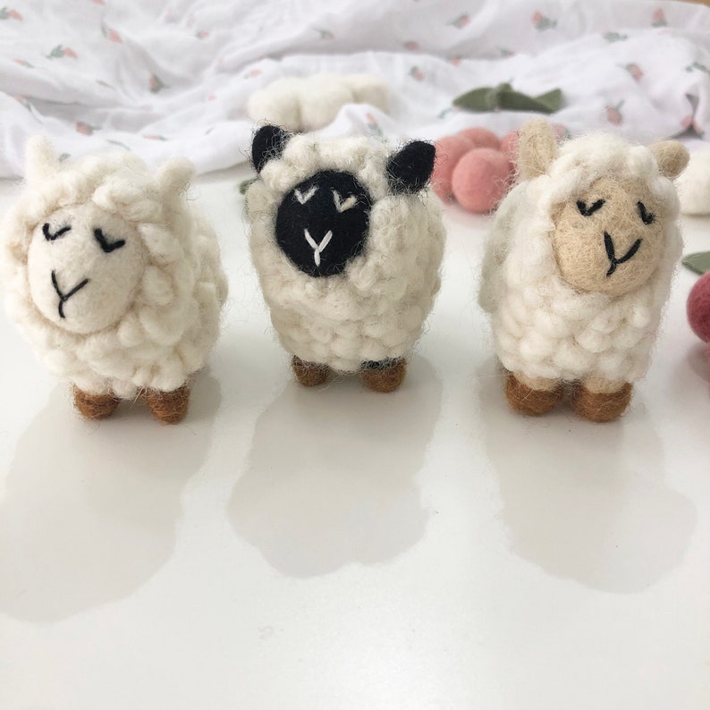 May include: Three white felt sheep toys with different facial features. One sheep has a black face, one has a brown face, and one has a white face.