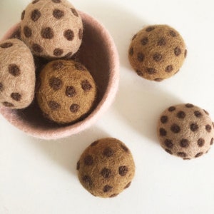 May include: Five brown felt balls with brown polka dots. The balls are in a light pink bowl and on a white surface.