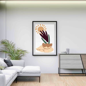 May include: Abstract art print in a black frame featuring a stylized sun, a plant with green and purple leaves, and a brown rock on a beige background.