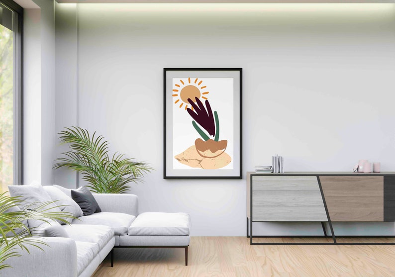 May include: Abstract art print in a black frame featuring a stylized sun, a plant with green and purple leaves, and a brown rock on a beige background.
