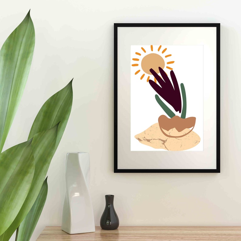 May include: A black framed print with a white background featuring a stylized illustration of a sun, a plant with purple and green leaves, and a brown rock. The illustration is in a minimalist style.