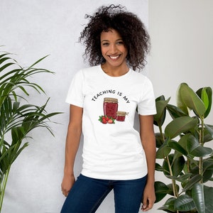 May include: White t-shirt with the text "Teaching is my jam" and a drawing of two jars of jam with strawberries.