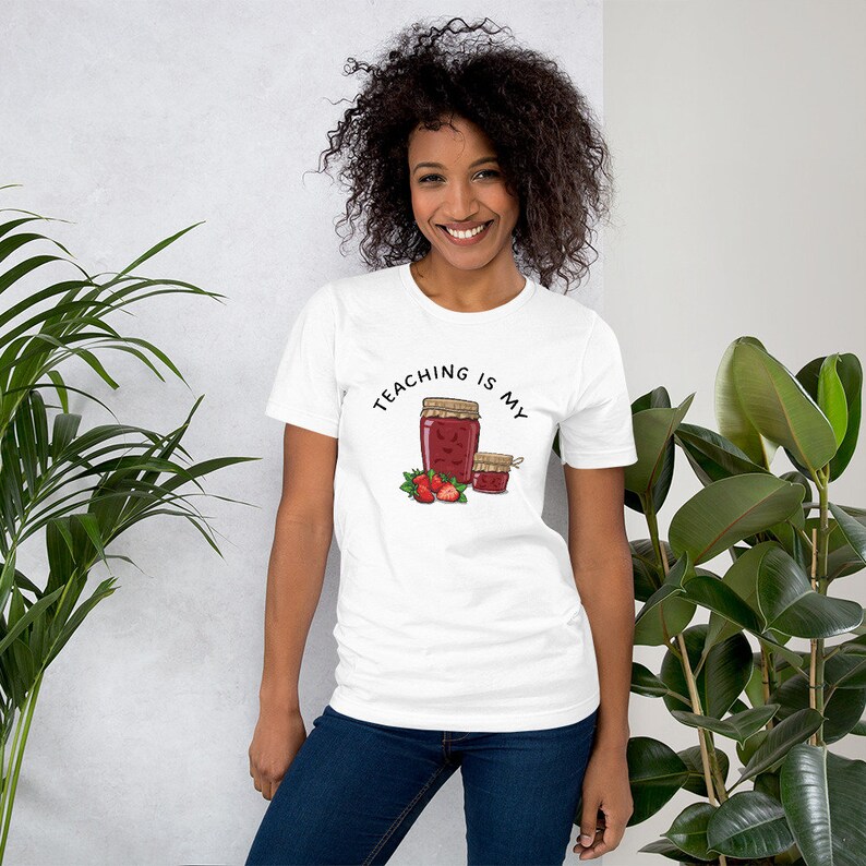 May include: White t-shirt with the text "Teaching is my jam" and a drawing of two jars of jam with strawberries.