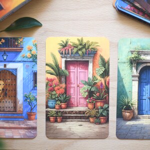 May include: Three rectangular art prints showcasing colourful illustrations of doorways. The prints depict doors in blue, pink, and green buildings, adorned with potted plants and architectural details. The artwork evokes a Mediterranean or Spanish aesthetic.