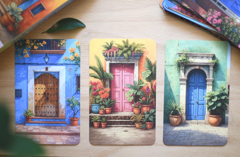 May include: Three rectangular art prints showcasing colourful illustrations of doorways. The prints depict doors in blue, pink, and green buildings, adorned with potted plants and architectural details. The artwork evokes a Mediterranean or Spanish aesthetic.
