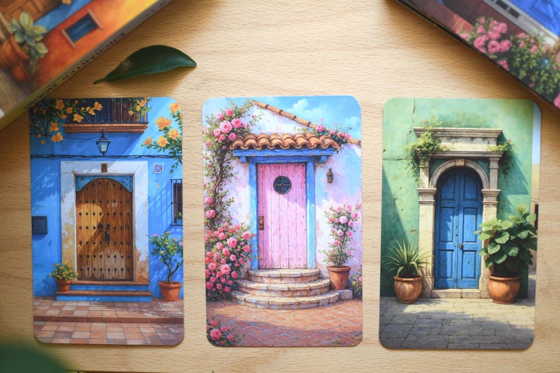 May include: Three rectangular art prints depicting watercolour illustrations of doors. One shows a blue building with a wooden door, another a pink door with flowers, and the last a green building with a blue door.