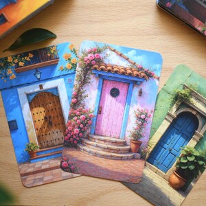 May include: Three art prints depicting doors with floral decorations. One shows a blue door with a wooden door, another a pink door with a tiled roof, and the last a blue door with a stone archway.