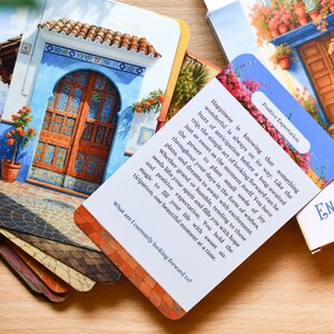 May include: A deck of "Enchanted Doors" oracle cards featuring images of doors and buildings. One card has text about positive expectation. The cards are displayed on a wooden surface.
