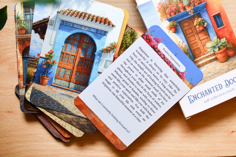 May include: A deck of "Enchanted Doors" oracle cards featuring images of doors and buildings. One card has text about positive expectation. The cards are displayed on a wooden surface.