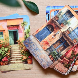 May include: A collection of illustrated cards showcasing architectural designs. The cards display buildings in vivid colours, such as orange, blue, and green, with intricate facades and potted plants. The cards are arranged on a light wooden surface.