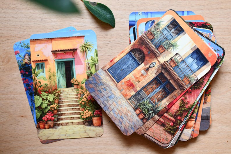 May include: A collection of illustrated cards showcasing architectural designs. The cards display buildings in vivid colours, such as orange, blue, and green, with intricate facades and potted plants. The cards are arranged on a light wooden surface.
