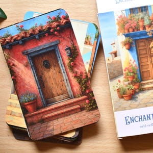 May include: A deck of "Enchanted Doors" oracle cards with colourful illustrations of doors and buildings. The cards depict architectural scenes with doors, flowers, and plants. The card box is white with blue text.