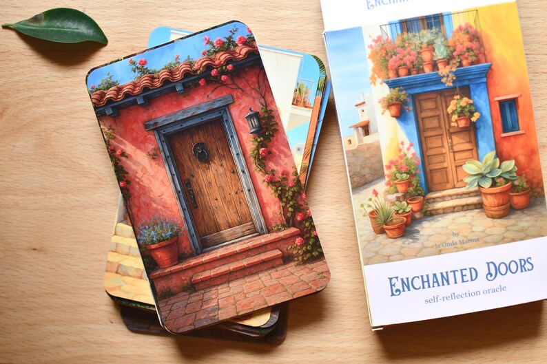 May include: A deck of "Enchanted Doors" oracle cards with colourful illustrations of doors and buildings. The cards depict architectural scenes with doors, flowers, and plants. The card box is white with blue text.