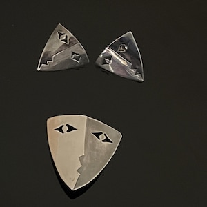 May include: A set of three silver earrings featuring geometric designs. The earrings are in the shape of triangles and a face.