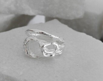 Könnte beinhalten: Ein silberner Ring mit organischem, strukturiertem Design. Der Ring besteht aus einem einzigen Stück Metall und hat eine einzigartige, asymmetrische Form.