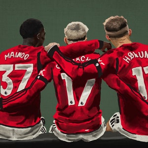 May include: Three soccer players in red jerseys with white numbers on the back. The player on the left has the number 37 and the name "Mainoo" on the back. The player in the middle has the number 17 and the name "Garnacho" on the back. The player on the right has the number 11 and the name "Holund" on the back.