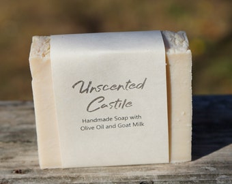 May include: A bar of unscented Castile soap wrapped in white paper with the text "Unscented Castile Handmade Soap with Olive Oil and Goat Milk".