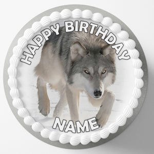 Könnte beinhalten: Ein runder Kuchen mit einem grauen Wolfsbild in der Mitte. Der Kuchen hat weißen Zuckerguss am Rand und die Worte "HAPPY BIRTHDAY" und "NAME" in schwarzem Text.