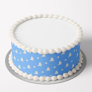 May include: A round cake with a smooth white top surface and a blue side wrap featuring a repeating pattern of small white clouds. The top and bottom edges of the cake are decorated with a continuous border of white piped frosting swirls.