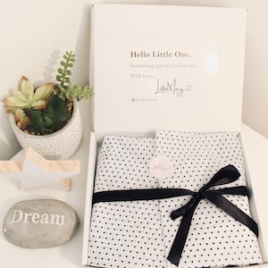 May include: A white gift box containing items wrapped in white tissue paper with black polka dots, secured by a black ribbon and a circular sticker. The inside lid features the text: Hello Little One, Something special just for you! With Love, Lottie May.