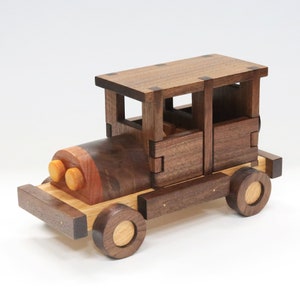 Può includere: Un'auto giocattolo di legno con un corpo marrone, un tetto marrone chiaro e ruote gialle. L'auto ha un interno dettagliato con finestre e porte.