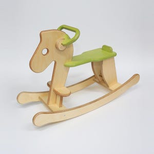 May include: A wooden rocking horse with a light green seat and handle. The horse is made of light-colored wood and has a classic design, perfect for young children. The rocking horse is approximately 30 inches long.
